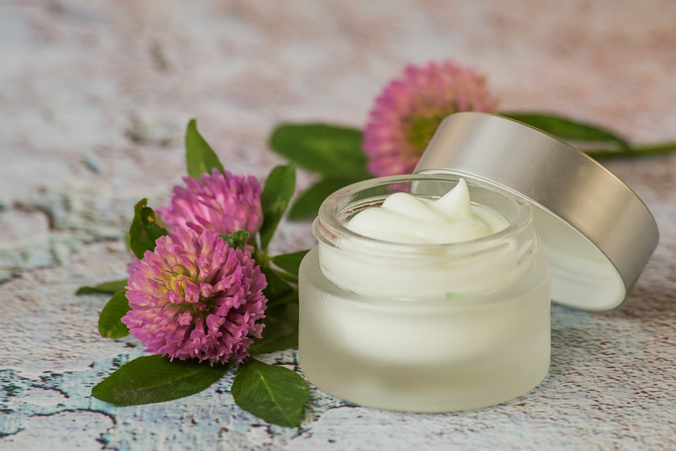 Natural cosmetic. A small glass jar with cream for skin care face and fresh clover flowers on a light background.